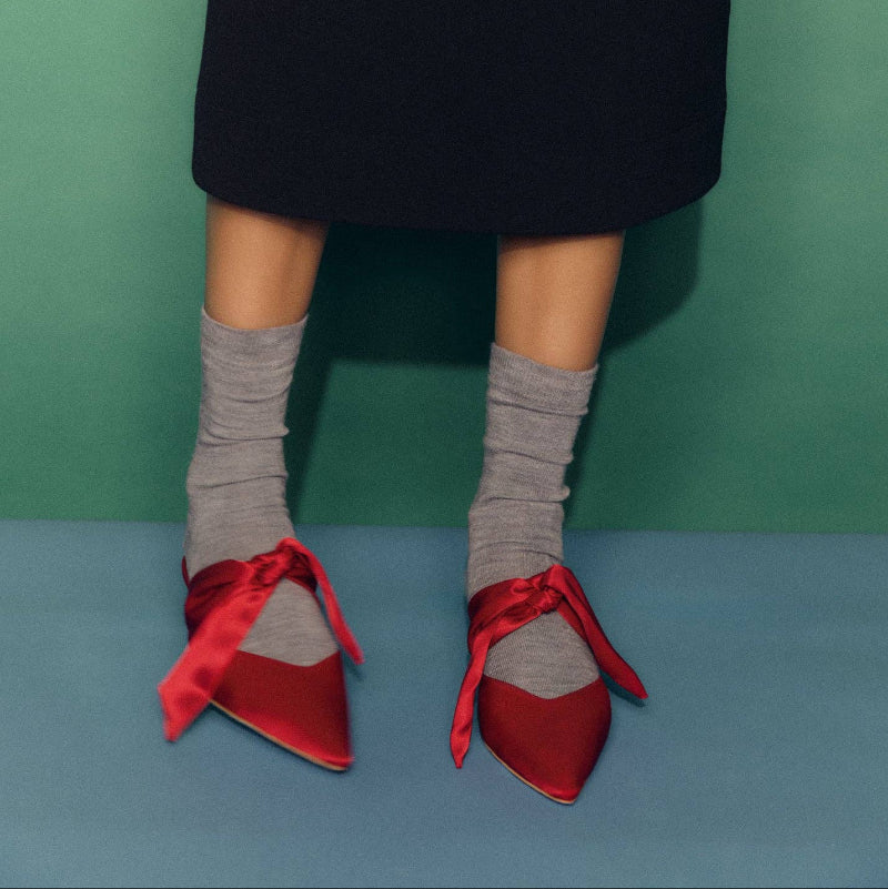 Red shoes with ribbons worn by a person against a green and blue background | Pairs Socks | Shop Fodder