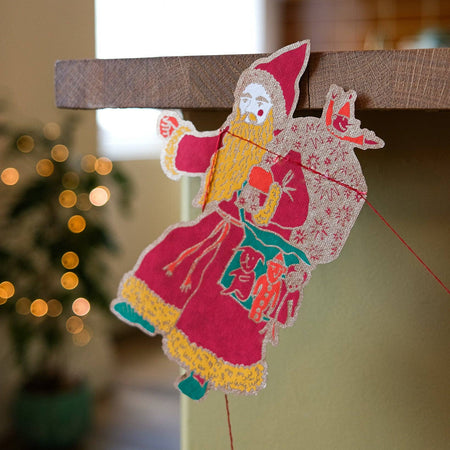 Decorative paper cutout of a traditional character on a wooden surface with blurred lights in the background. East End Press | Shop Fodder