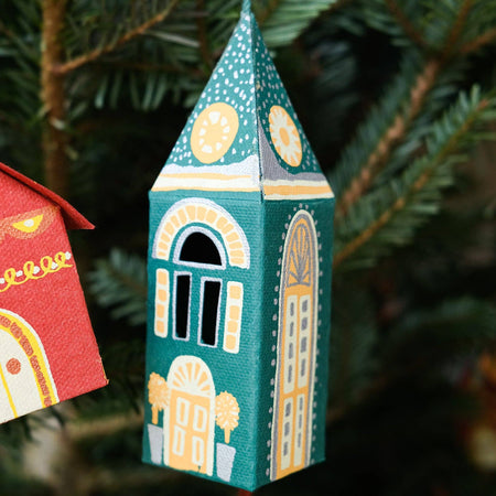 Decorative Christmas ornament shaped like a building with a green roof and yellow accents, hanging on a tree. East End Press | Shop Fodder