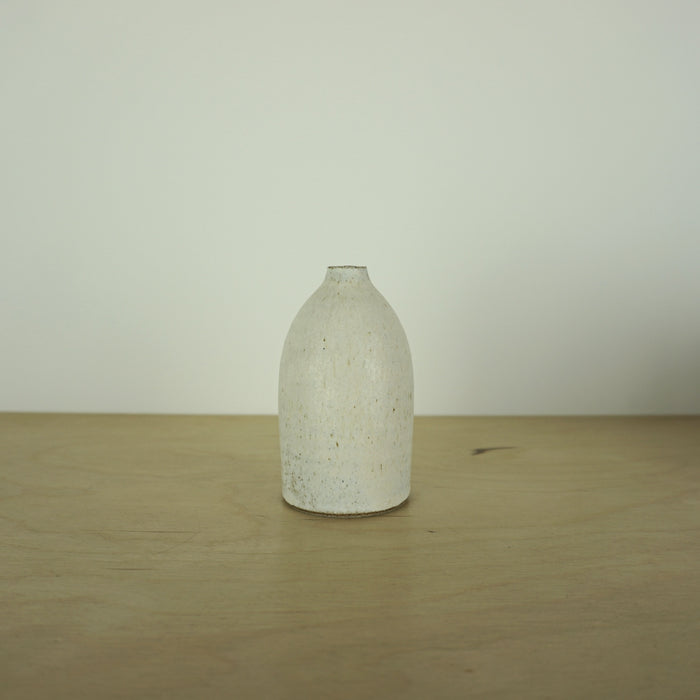 a small ivory coloured white handmade ceramic vase on a table. 
