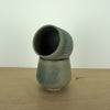 small handmade blue green cup, sitting on an angle inside another cup on a wooden table and a white background. 