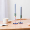 two glass candlestick holders on a table with a jug and salt dish 