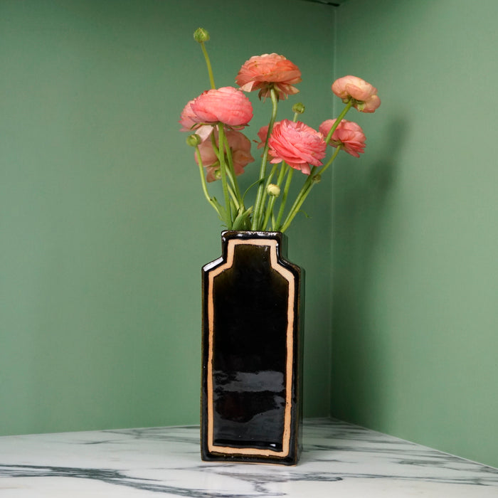 deep glossy black vase with pink flowers on a green background. 