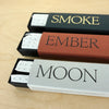 three open packets of incense sticks on a table. one called moon, one called ember and one called smoke. 