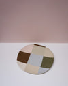 Round patchwork rug with multicolored squares on a white surface and pink background. Patchwork Platter | Brutes London | Handmade Ceramics | Fodder