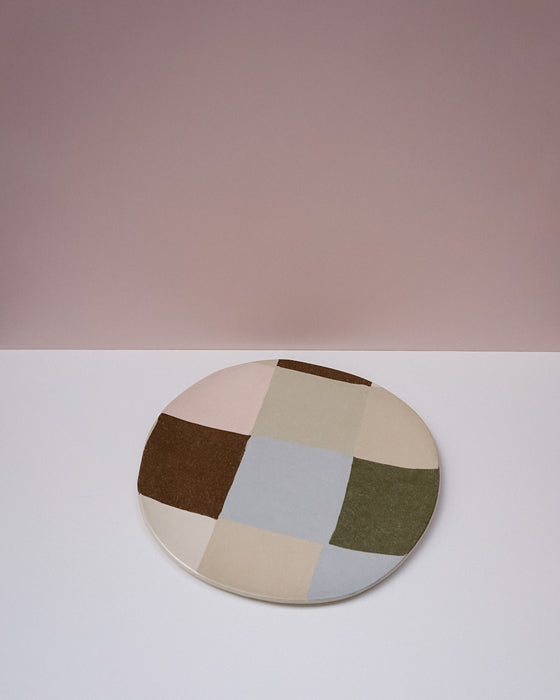 Round patchwork rug with multicolored squares on a white surface and pink background. Patchwork Platter | Brutes London | Handmade Ceramics | Fodder