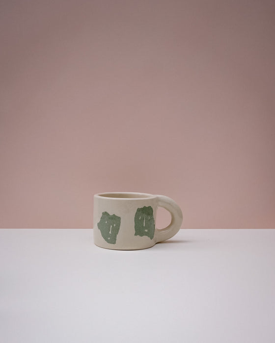 White mug with green designs on a pink background. Portrait Mug | Brutes London | Handmade Ceramics | Fodder