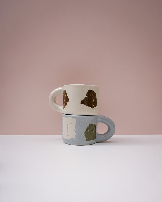 Two ceramic mugs stacked on a white surface with a pink background. Portrait Mug | Brutes London | Handmade Ceramics | Fodder