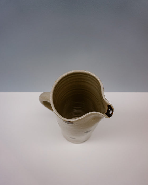Ceramic pitcher on a white surface with a grey background. Water jug by Cara Guthrie - iron wash dots - handmade stoneware - Fodder
