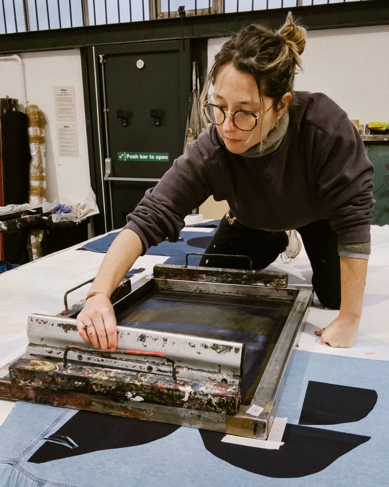 Person working with a screen printing frame in an industrial setting. Caroline Dickinson handprinting shirts in the studio