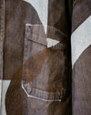 Close-up of a brown denim jacket featuring a large chest pocket with a unique triangular stitched detail, set against a matching abstract geometric patterned fabric. Caroline Dickinson Shirt | Fodder