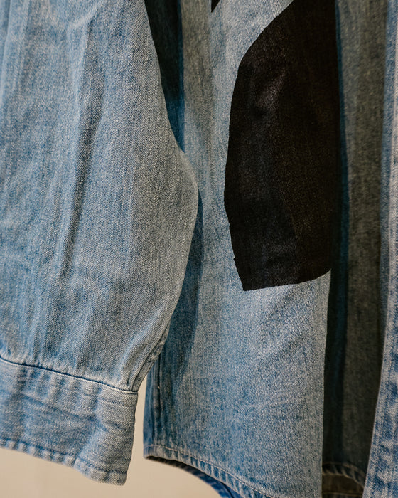 Close-up of a light blue denim jacket featuring a large black fabric patch on the chest. Caroline Dickinson Shirt | Fodder