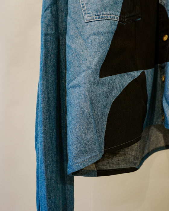 A close-up of a patchwork denim jacket featuring blue and black fabric panels, with a visible button closure and pocket detail. Caroline Dickinson Shirt | Fodder