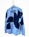 A long-sleeve button-up shirt with a light blue and dark navy blue patchwork design, hanging on a white hanger against a plain white background. Caroline Dickinson Shirt | Fodder