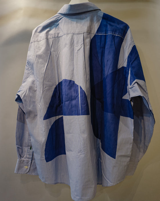 A light blue chambray button-down shirt with a bold blue geometric block print pattern, shown from the back on a mannequin against a neutral beige background. Caroline Dickinson Shirt | Fodder