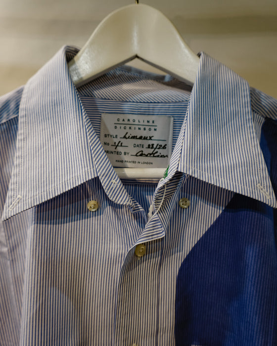A close-up of a Caroline Dickinson shirt on a white hanger, featuring a blue and white striped pattern on the upper chest and a solid dark blue panel on the lower right. Caroline Dickinson Shirt | Fodder