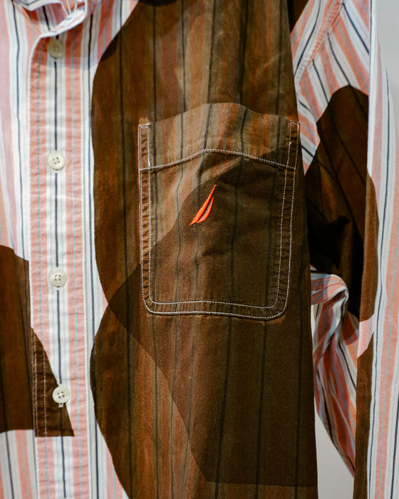 A close-up of a brown corduroy vest layered over a pink, white, and blue striped button-down shirt. The vest features a chest pocket with white contrast stitching and a small orange embroidered sail logo. Caroline Dickinson Shirt | Fodder