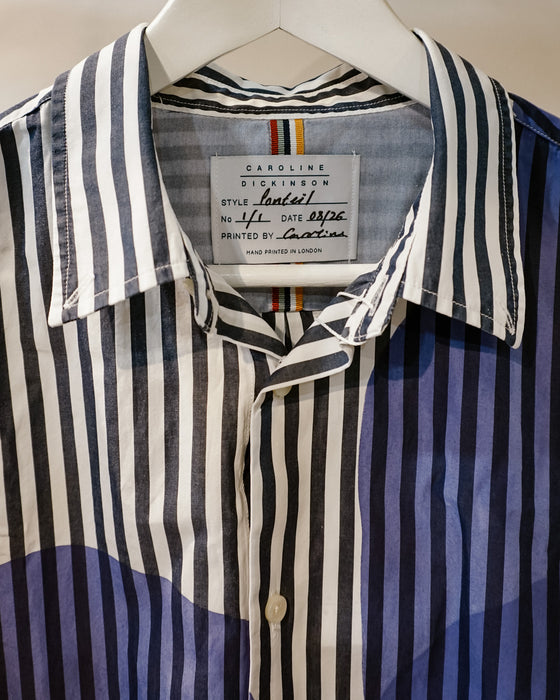 A close-up of a Caroline Dickinson shirt on a white hanger, featuring vertical stripes in navy blue, white, and black, with a blue and white abstract pattern on the lower half. Caroline Dickinson Shirt | Fodder