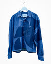 A blue patchwork patterned long-sleeve button-up shirt hanging on a white hanger against a plain white background. Caroline Dickinson Shirt | Fodder