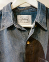 A close-up of a denim shirt jacket hanging on a white hanger, showing a collar, front button placket, and a sewn-in label that reads Caroline Dickinson Style Redfield No. 1. Caroline Dickinson Shirt | Fodder