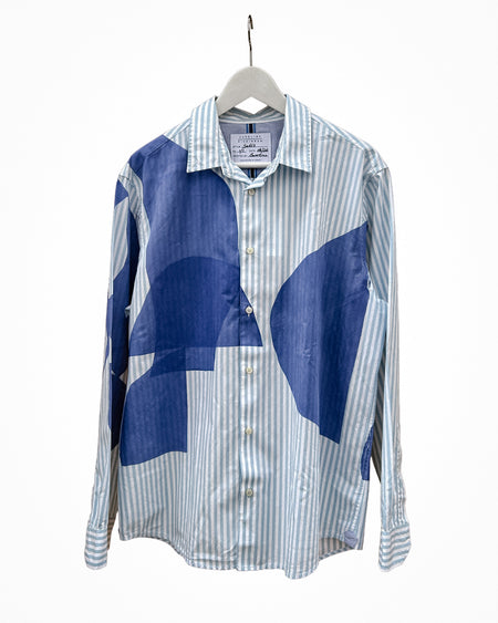 A long-sleeve button-up shirt hanging on a white hanger against a plain white background. The shirt features a blue and white striped base with large abstract blue color-block panels on the front. Caroline Dickinson Shirt | Fodder