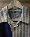 A close-up of a Caroline Dickinson shirt on a white hanger, featuring a light blue and white striped pattern on the upper portion and a solid dark navy blue panel on the lower left. Caroline Dickinson Shirt | Fodder