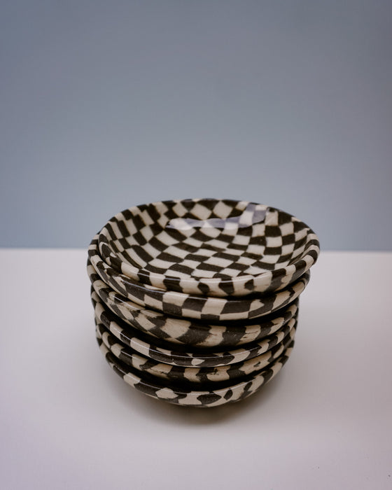 Stack of black and white checkered bowls on a white surface with a grey background