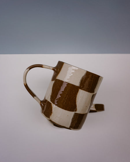 Ceramic mug with brown and beige checkered pattern on a white surface with gray background. Checkerboard Nerikomi Ceramic Mug | Fern Taylor | Kentish Town Stores