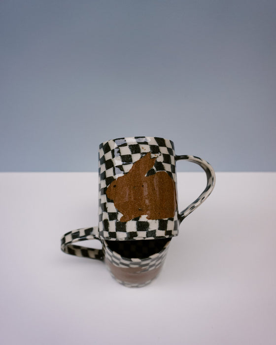Ceramic mug with checkered pattern and brown abstract design on a white surface. Bunny Mugs by Ceramicist Fern Taylor | Shop Fodder