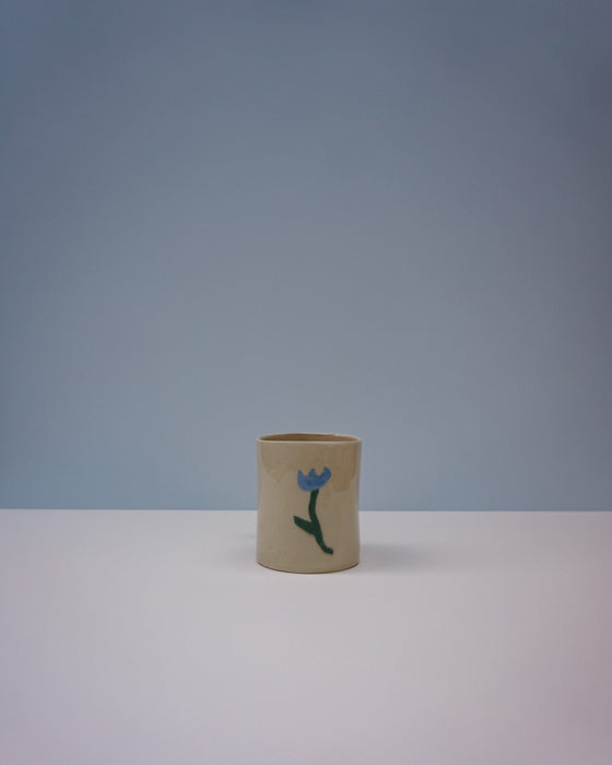 Small cylindrical ceramic vase with a blue flower design on a light gray background. Tulip Mug | Nerikomi | Fern Taylor | Shop Fodder