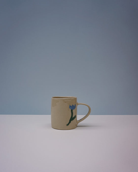 Beige mug with a blue flower design on a light grey background. Tulip Mug | Nerikomi | Fern Taylor | Shop Fodder