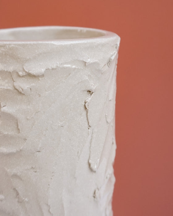 A close-up of a textured, off-white ceramic pot or vase with a rough, hand-painted plaster-like finish, set against a solid terracotta background.  Brutes Ceramics | Hope Collection | Shop Fodder