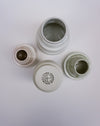 Four small ceramic jars with matching lids arranged on a plain white background. One jar is open at the top, one lid is shown upside down with a visible circular logo reading 'ESMA JOHAN CEBANCI' and 'CEMENT', one lid is off showing the inside, and one jar is partially open.  Emma Johnson Ceramics | Fodder | Hope Collection