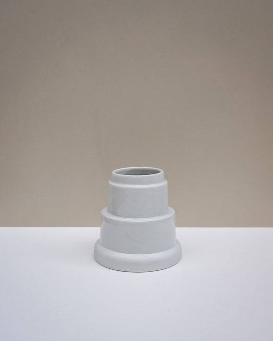 A small white ceramic vase with a tiered, stepped design, set on a white surface against a warm beige background. Emma Johnson Ceramics | Fodder | Hope Collection