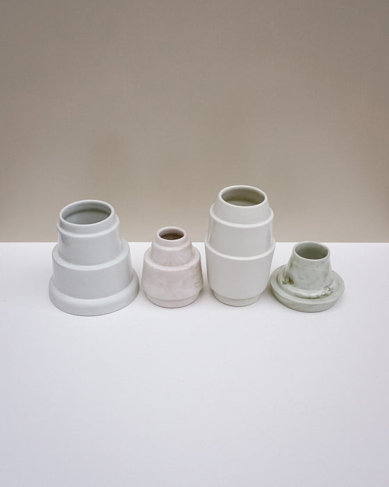 Four small ceramic vases in different glazes and shapes arranged on a white surface against a warm beige. Emma Johnson Ceramics | Fodder | Hope Collection