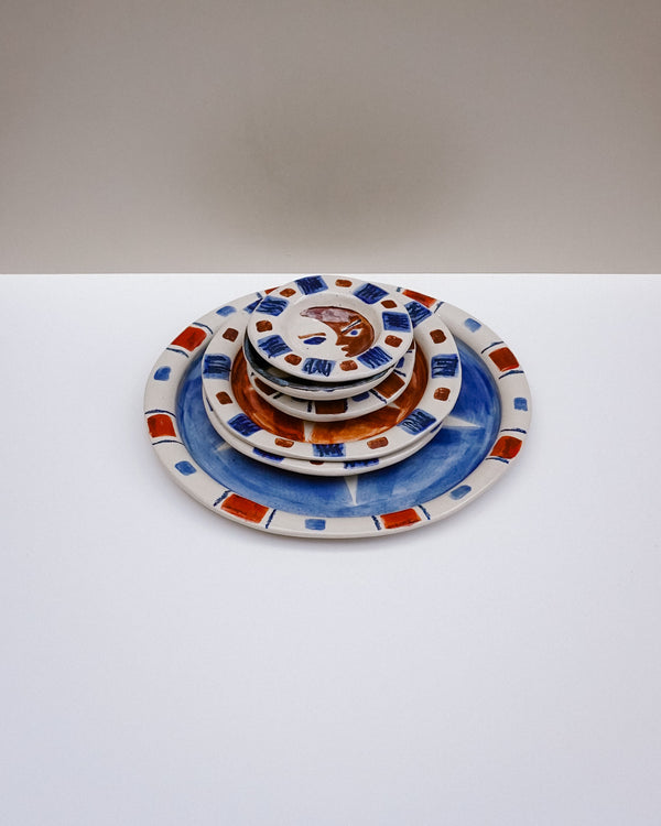 A stack of five nested ceramic plates with a hand-painted Majolica style design, featuring blue, terracotta orange, and white with small red accents. Hoodmor Studio | Fodder | Hope Collection