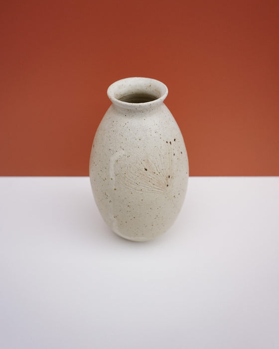 A small handmade ceramic vase with a speckled cream glaze and a subtle hand-painted floral motif on the front, set against a split orange and white background. KJA Studio Ceramics | Hope Collection | Shop Fodder