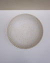 A round ceramic bowl with a speckled beige and brown glaze, photographed from directly above on a white surface with a beige background strip at the top. Scree Ceramics | Fodder | Hope Collection