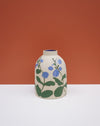 A ceramic vase with a rounded body, featuring a hand-painted blue and green floral pattern on a cream-colored stoneware surface, set against a split orange and white background. Sophie Alda | Hope Collection | Shop Fodder