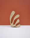 A minimalist abstract ceramic sculpture with a light natural wood finish, displayed on a white surface against a terracotta-colored background. Studio ERS Ceramics | Hope Collection | Shop Fodder