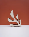 A minimalist abstract wooden sculpture with organic, leaf-like cutouts, standing on a white surface against a terracotta-colored background. Studio ERS Ceramics | Hope Collection | Shop Fodder