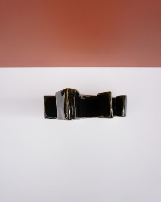 A glossy black ceramic planter with a geometric, tiered design, photographed from directly above on a white surface with a terracotta-colored background in the upper half. Studio ERS Ceramics | Hope Collection | Shop Fodder