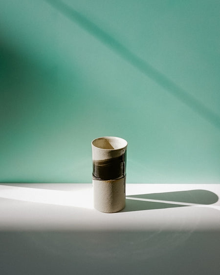 Cylindrical ceramic vase with two-tone design on a light surface with a teal background.  Janne Meijer Ceramics | Shop Fodder