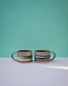 Two ceramic mugs with striped design on a light blue surface and teal background.  Janne Meijer Ceramics | Shop Fodder