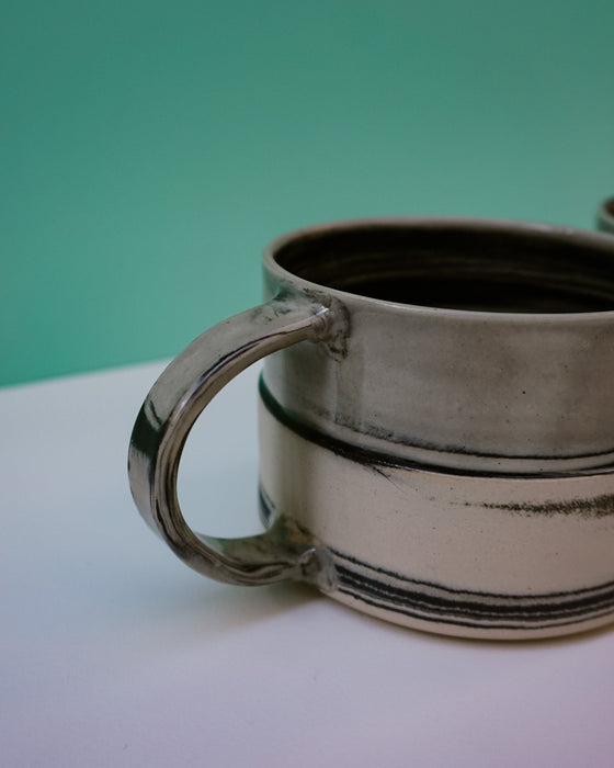 Ceramic mug with a handle on a white surface against a green background.  Janne Meijer Ceramics | Shop Fodder