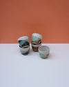 Set of ceramic cups with striped patterns on a white surface and orange background. Liz Vidal Ceramics | Shop Fodder