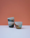 Two ceramic cups with geometric patterns on a white surface and orange background. Liz Vidal Ceramics | Shop Fodder