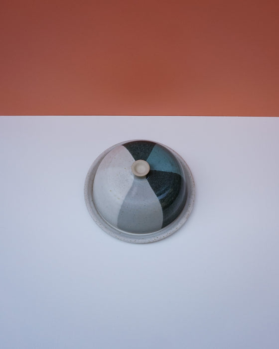 Ceramic jar with a lid on a white surface with an orange background. Liz Vidal Ceramics | Shop Fodder