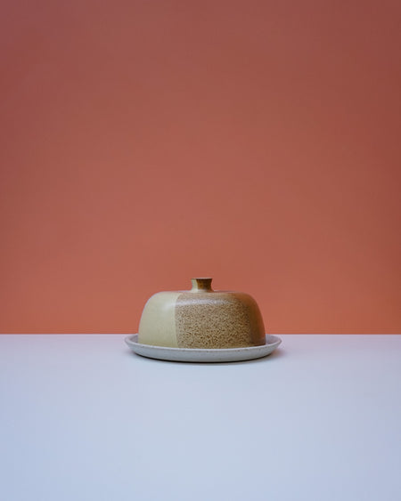 Ceramic butter dish with a textured surface on a white plate against a peach background. Liz Vidal Ceramics | Shop Fodder