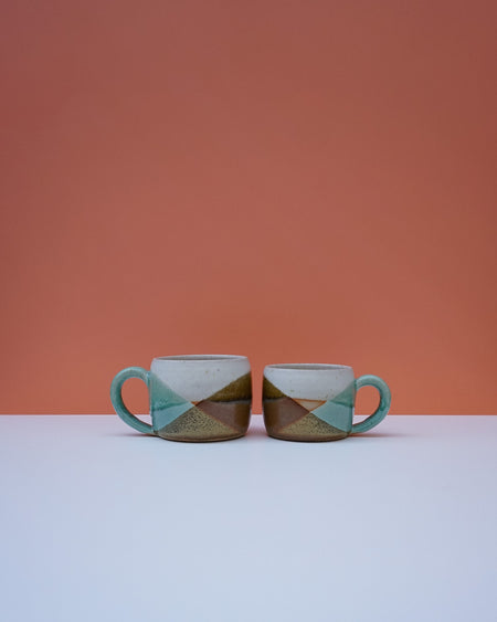 Two ceramic mugs with geometric pattern on a white surface and orange background. Liz Vidal Ceramics | Shop Fodder